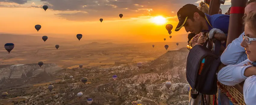 People looking over hot-air balloon basket over Cappadocia at sunrise