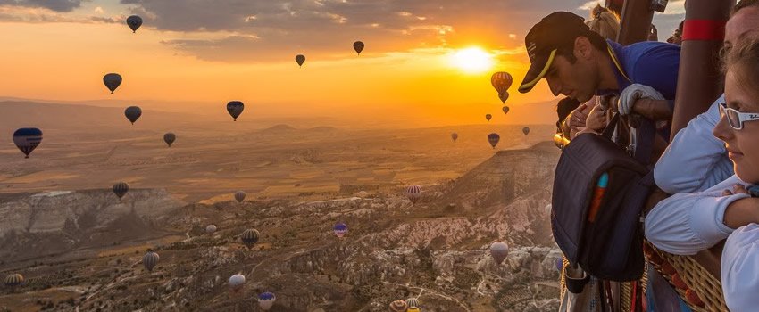 People looking over hot-air balloon basket over Cappadocia at sunrise